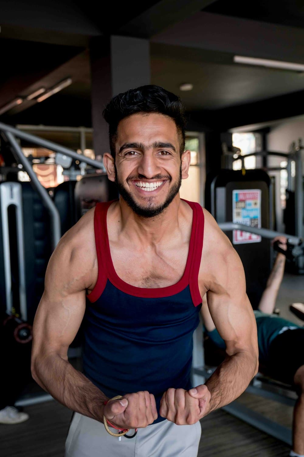 Portrait of a smiling, muscular male coach in a tank top inside a gym